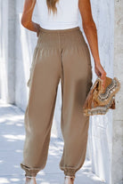 Boho Dreamer high-waist elastic pants in beige with a stretchy waistband and cuffed ankles worn with a white top and holding a boho-style bag.