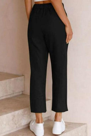 Woman wearing black relaxed fit straight pants with white sneakers, shown from back