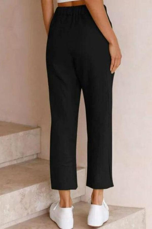 Woman wearing black relaxed fit straight pants with white sneakers, shown from back