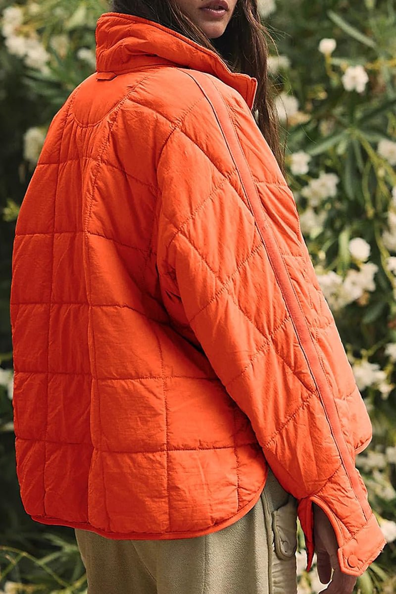Orange lightweight puffer travel jacket with quilted design and high collar, worn outdoors.