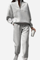 Woman wearing gray cotton-blended two-piece tracksuit with high collar and zipper, holding a cup.