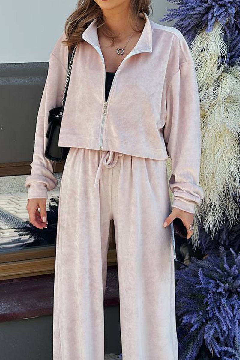 Woman wearing a soft pink zip up cropped sweatshirt and wide leg velour pants leisure two-piece co-ord set.