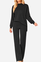 Woman wearing a black high neck sweater and wide leg pant set with long sleeves and knit cuffs