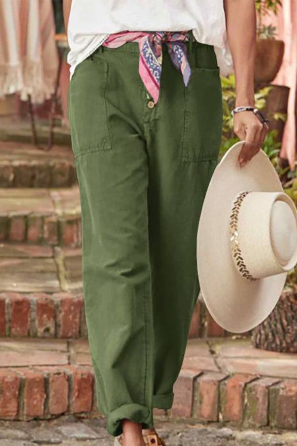 Woman wearing casual button-down utility-chic green trousers with pockets and rolled cuffs, holding a beige hat.