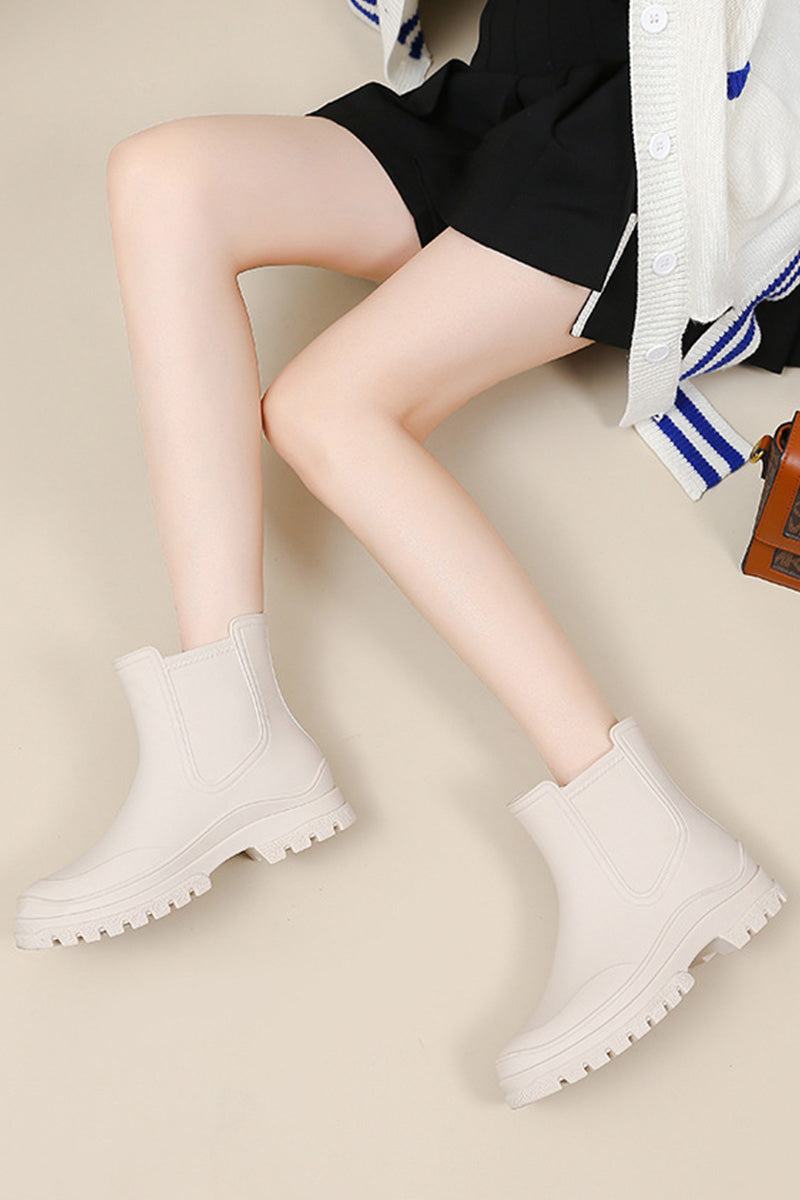 Light beige non-slip rain boots with chunky soles worn with black shorts and a white cardigan
