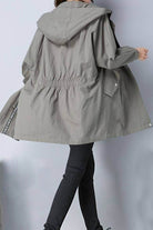 Back view of a gray fashion hooded trench coat with oversized silhouette and cinched waist, worn with black pants.