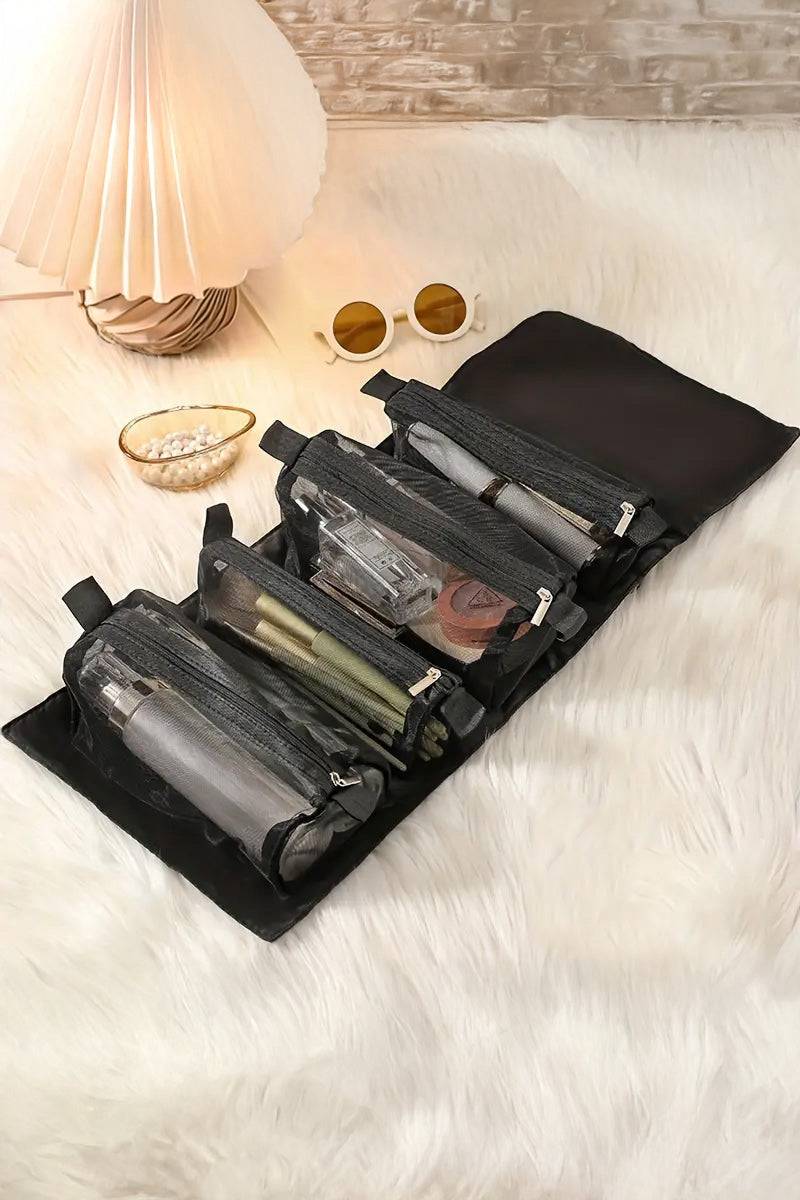 Compact black nylon travel makeup bag with multiple compartments and zipper pockets for organized cosmetics, laid open on a white furry surface next to sunglasses and lamp, designed for travel light look right.