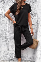Woman wearing black cotton Total Comfort Two-Piece Set with short sleeves and drawstring pants against textured wall