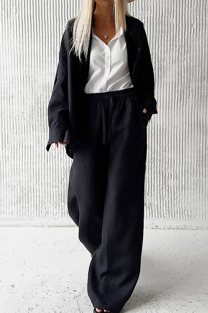 Woman wearing 100 Cotton Wanderlust black two-piece cotton set with white blouse against textured wall background