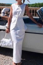 Woman wearing white cotton-linen blend sleeveless vest and high-waisted skirt two-piece outfit standing next to a vintage car