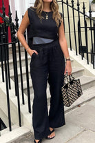 Woman wearing black cotton-linen blend sleeveless crop top and wide-leg pants holding a geometric patterned handbag outdoors