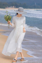 woman wearing white 100 linen coastal shift dress and sun hat walking on the beach holding flowers