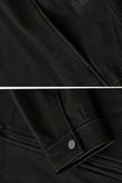 Close-up of black sheepskin leather jacket texture and sleeve detail with snap button, showcasing genuine soft leather material.