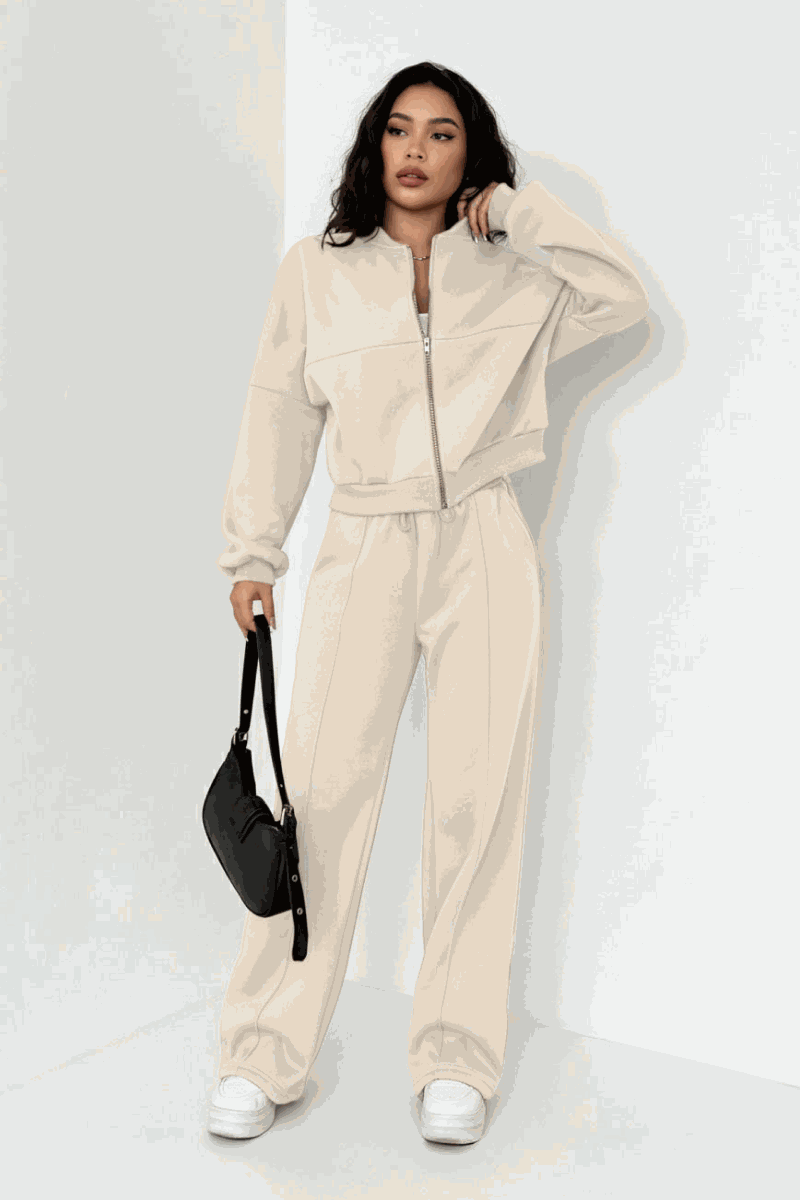 Woman wearing beige Voyager Zip Set with zip-front sweatshirt and wide-leg joggers, styled with white sneakers and black handbag.