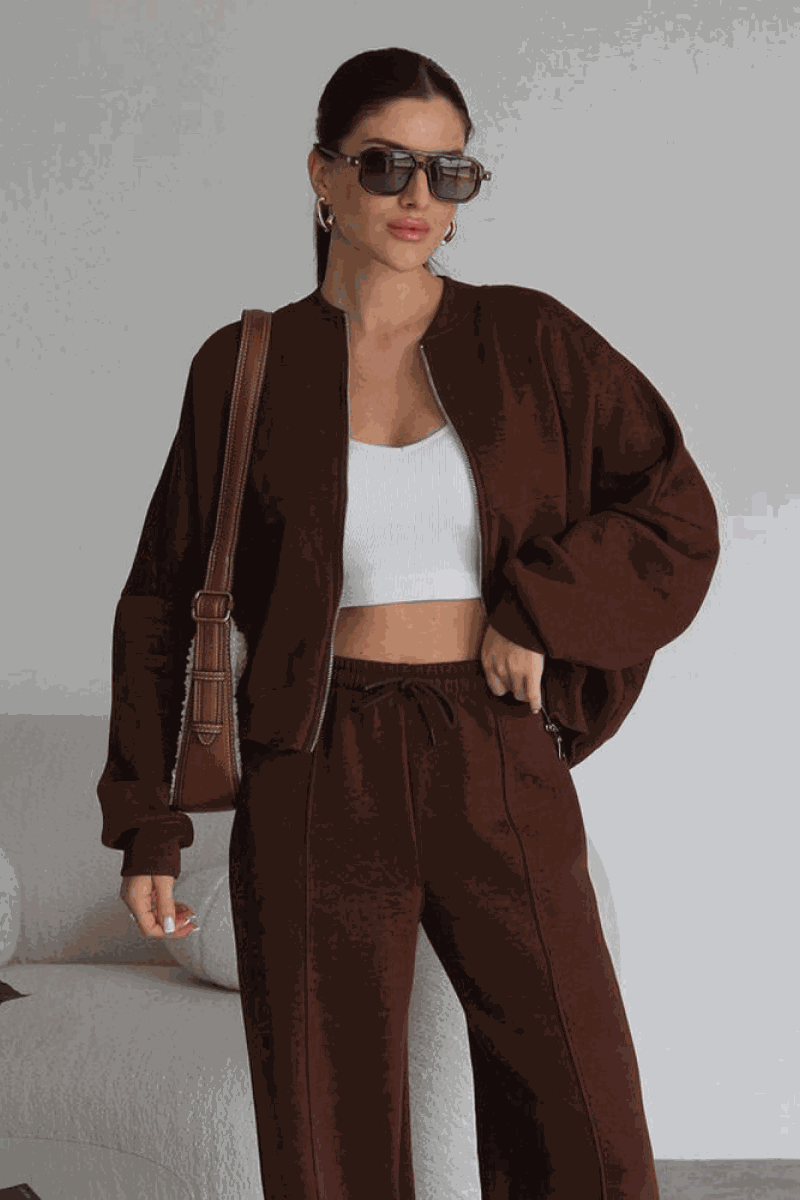 Woman wearing The Voyager Zip Set brown zip-front sweatshirt and wide-leg joggers with pockets, styled with sunglasses and a shoulder bag.