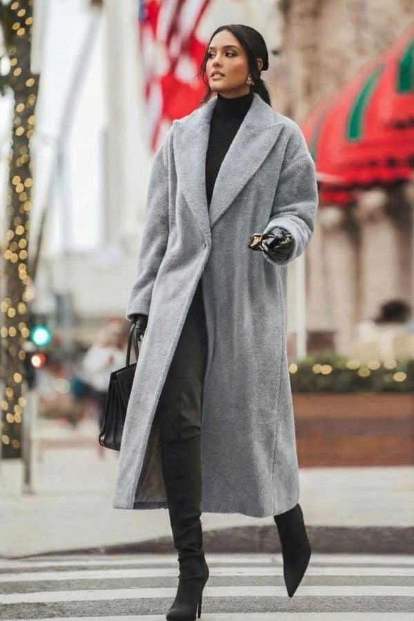 Woman wearing long grey oversized teddy coat with oversized lapels and black high-heeled boots walking on city street