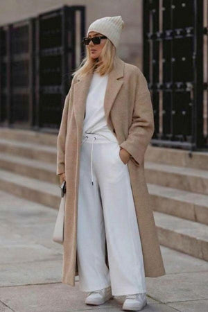 Woman wearing beige oversized teddy coat with white pants and beanie walking outdoors