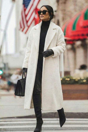 Woman wearing white oversized teddy coat with longline silhouette and black accessories on city street
