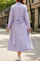 woman wearing a lavender timeless retro belted trench coat walking on city street, back view