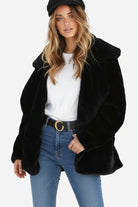 Woman wearing open front oversized black faux fur jacket with draped collar and relaxed fit