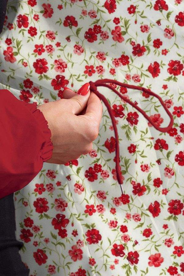 Close-up of hand adjusting drawstring on red water-resistant windbreaker against floral background