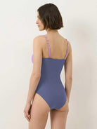 Gold-detail cutout one-piece swimsuit with ruched panels and gold dome accent, paired with a midi wrap skirt for beach coverage
