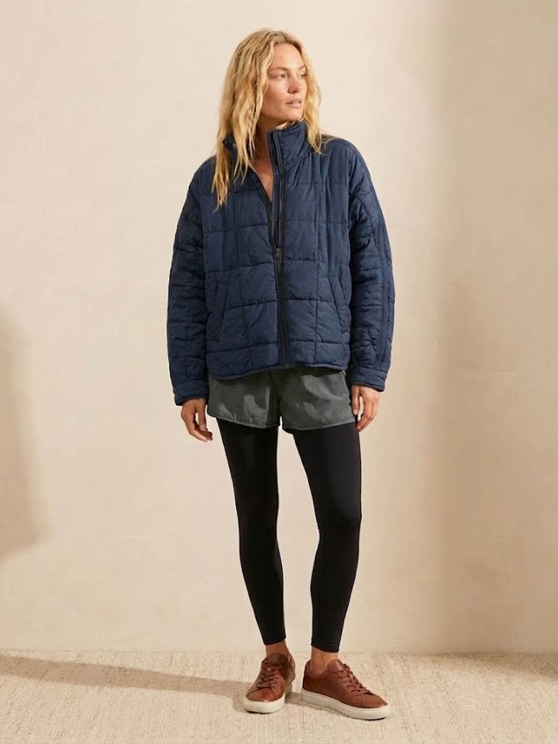 woman wearing navy lightweight puffer travel jacket with black leggings and brown sneakers