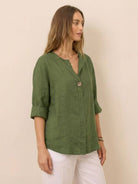 Woman wearing green Pure Linen Age-Defying Shirt with button details and rolled sleeves paired with white pants