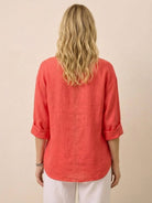 Back view of woman wearing coral Pure Linen Age-Defying Shirt with rolled sleeves and white pants