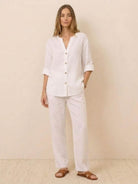 Woman wearing a white pure linen age-defying button detail shirt and matching linen pants with brown sandals.