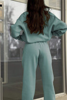 Woman wearing mint green Classic Airplane Set two-piece tracksuit from the back, standing indoors near glass door.
