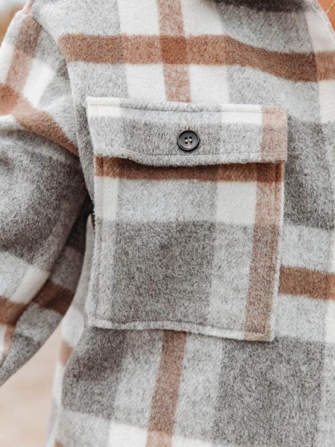 Close-up of a comfy flannel classic shirt pocket in gray, white, and brown plaid pattern with button detail