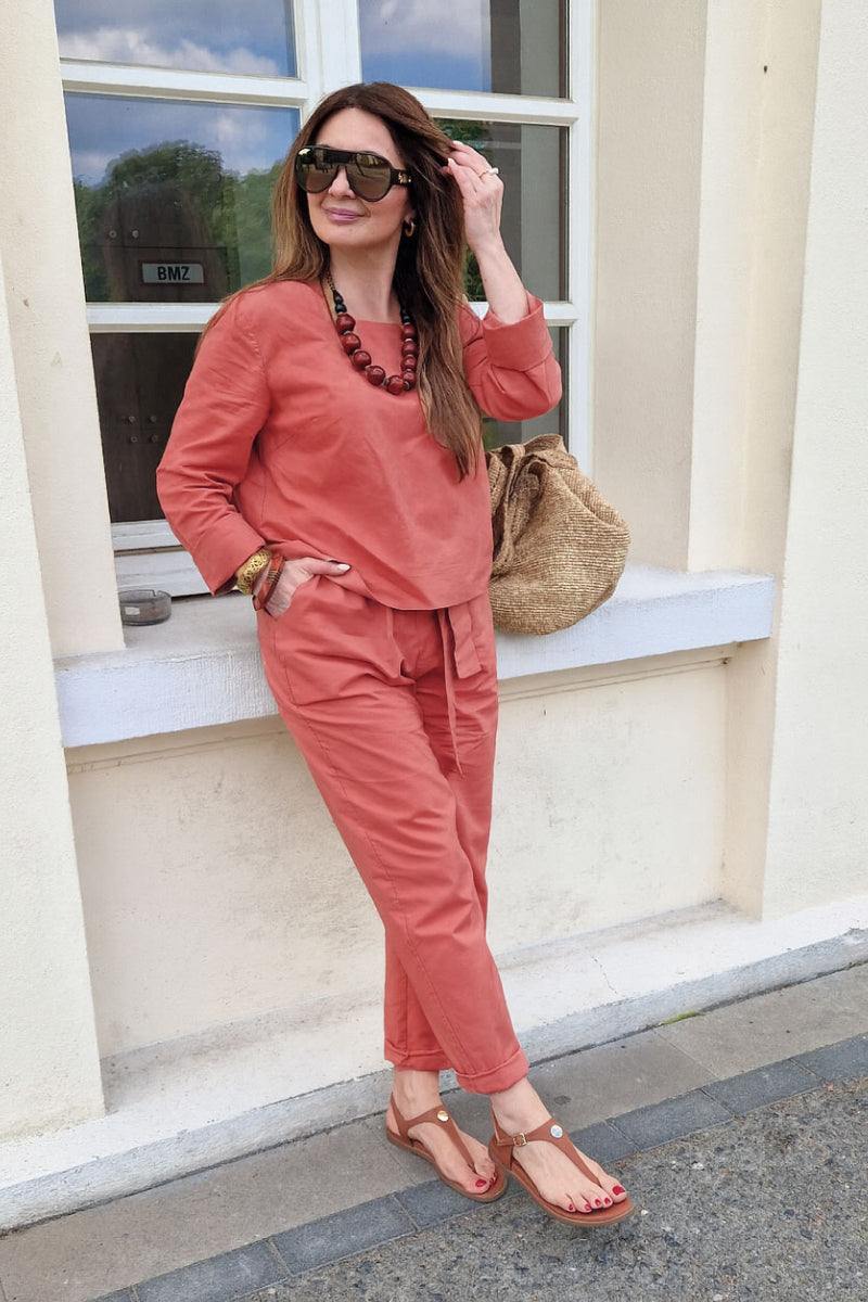 Woman wearing relaxed cotton-linen monochrome longline top and wide-leg pants set in terracotta color with sunglasses and accessories outdoors