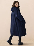 Woman wearing oversized navy waterproof windbreaker jacket with hood and pockets, longline design for layering and weather protection