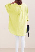 Back view of a bright yellow oversized linen shirt with loose sleeves and gathered detailing at the yoke, worn over white pants, styled for a relaxed fit.