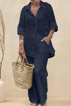 Woman wearing oversized 100% cotton shirt and wide-leg pants co-ord set in dark navy blue with rolled sleeves and carrying a woven basket bag.