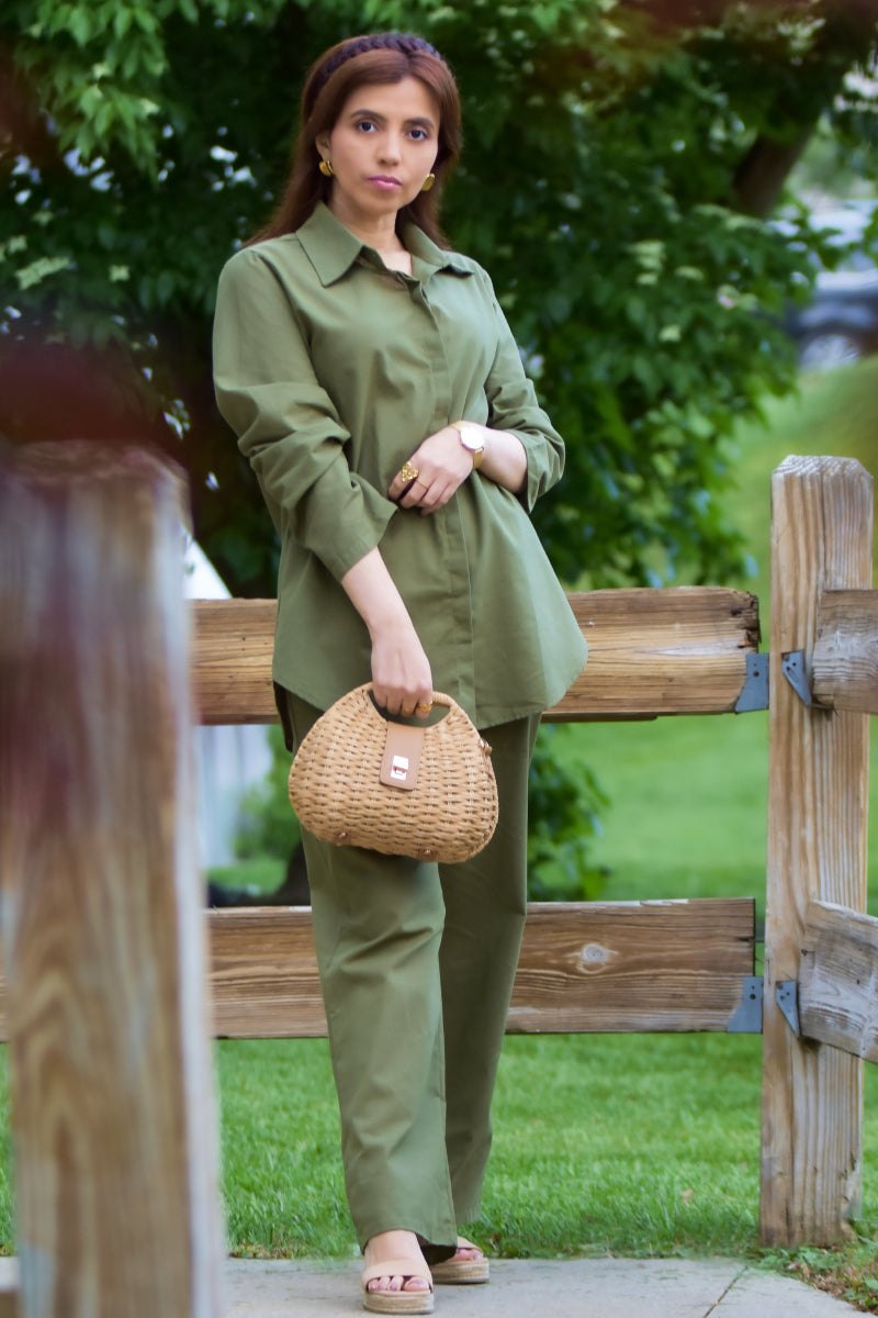 Woman wearing oversized 100% cotton olive green shirt and wide-leg pants set holding a woven handbag outdoors