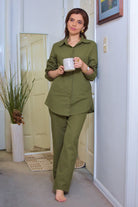 Woman wearing oversized 100% cotton olive green shirt and wide-leg pants co-ord set indoors holding a mug