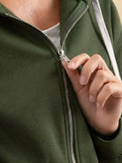 Close-up of hand zipping up oversized long zip sweatshirt hoodie in olive green fleece material