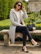 Woman wearing Sherpa-lined hooded teddy coat sitting on stone bench outdoors with sunglasses and handbag nearby