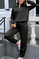 Woman wearing black cotton blend tracksuit with zip neckline and cuffed pants, holding coffee cup outdoors