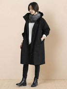 Woman wearing black oversized Rain Couture Windbreaker with scarf and boots against beige background