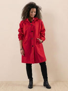 Woman wearing bright red Rain Couture Windbreaker water-resistant oversized jacket with black leggings and boots