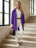 Woman wearing purple Rain Couture Windbreaker with white pants and carrying brown handbag indoors