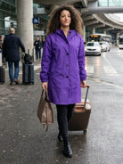 Woman wearing purple Rain Couture Windbreaker walking with luggage on city street