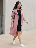 Woman wearing trendy oversized pink Rain Couture Windbreaker over black dress with white sneakers walking outdoors