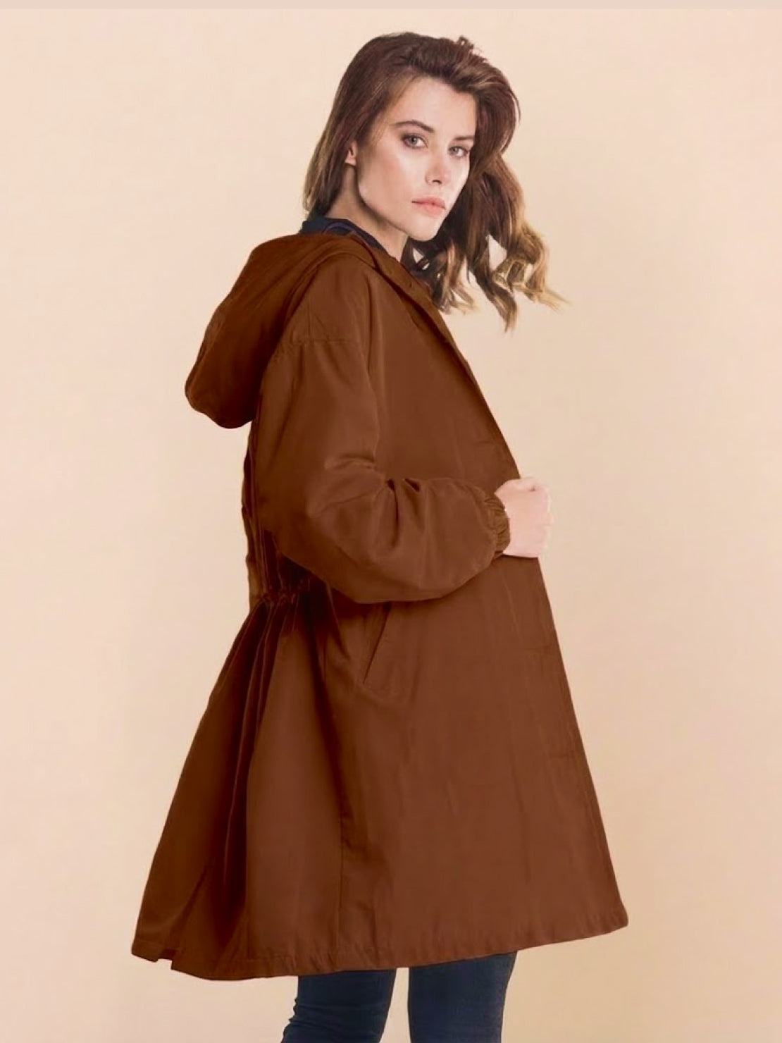 Woman wearing oversized brown Rain Couture Windbreaker rain jacket with hood against beige background
