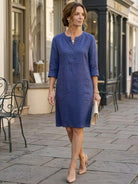 Woman wearing a knee-length blue cotton dress with rolled ¾ sleeves and a half-button front walking on a city street
